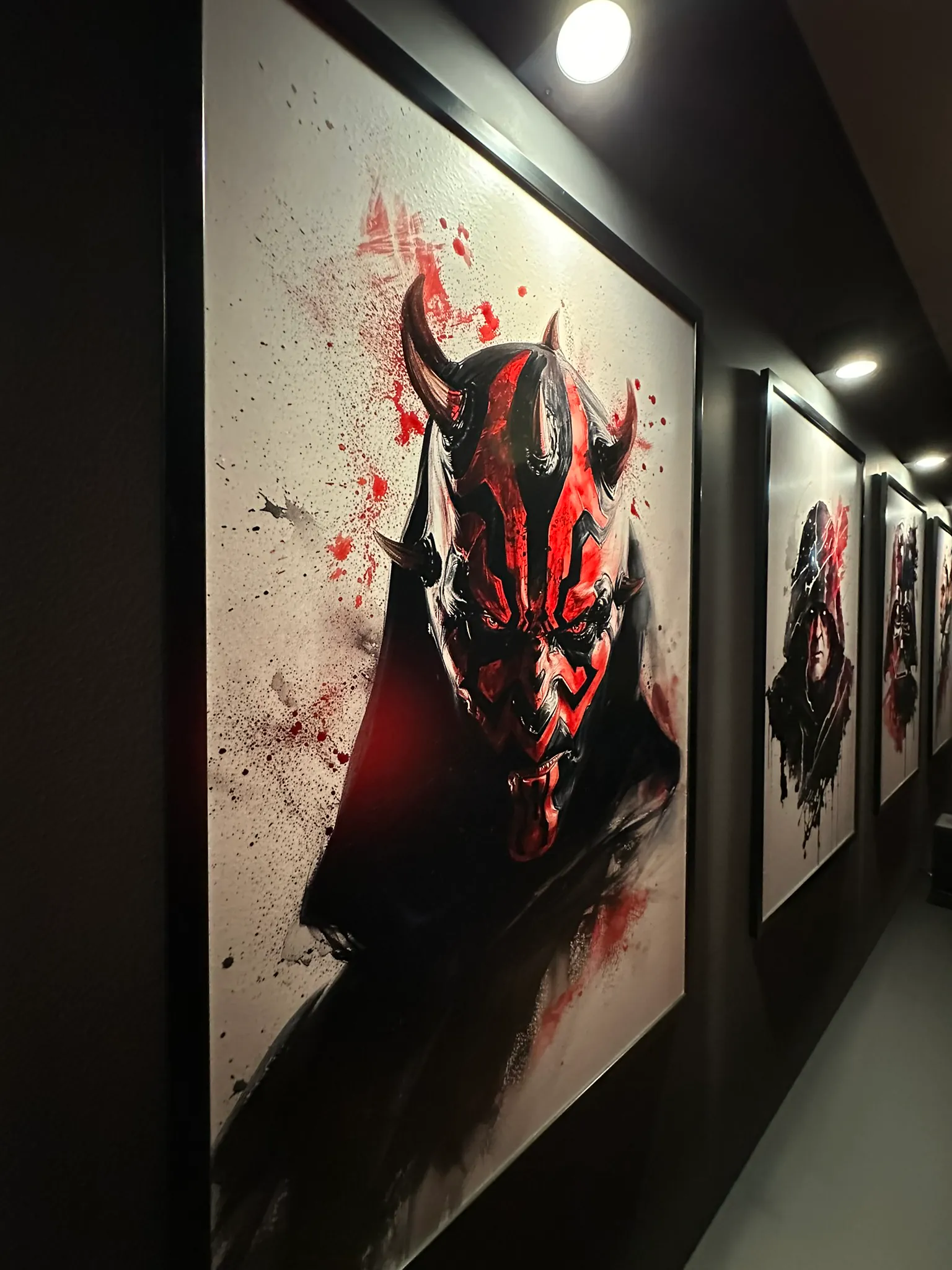 A dark corridor hung with framed prints, each lit by its own downlight from above.