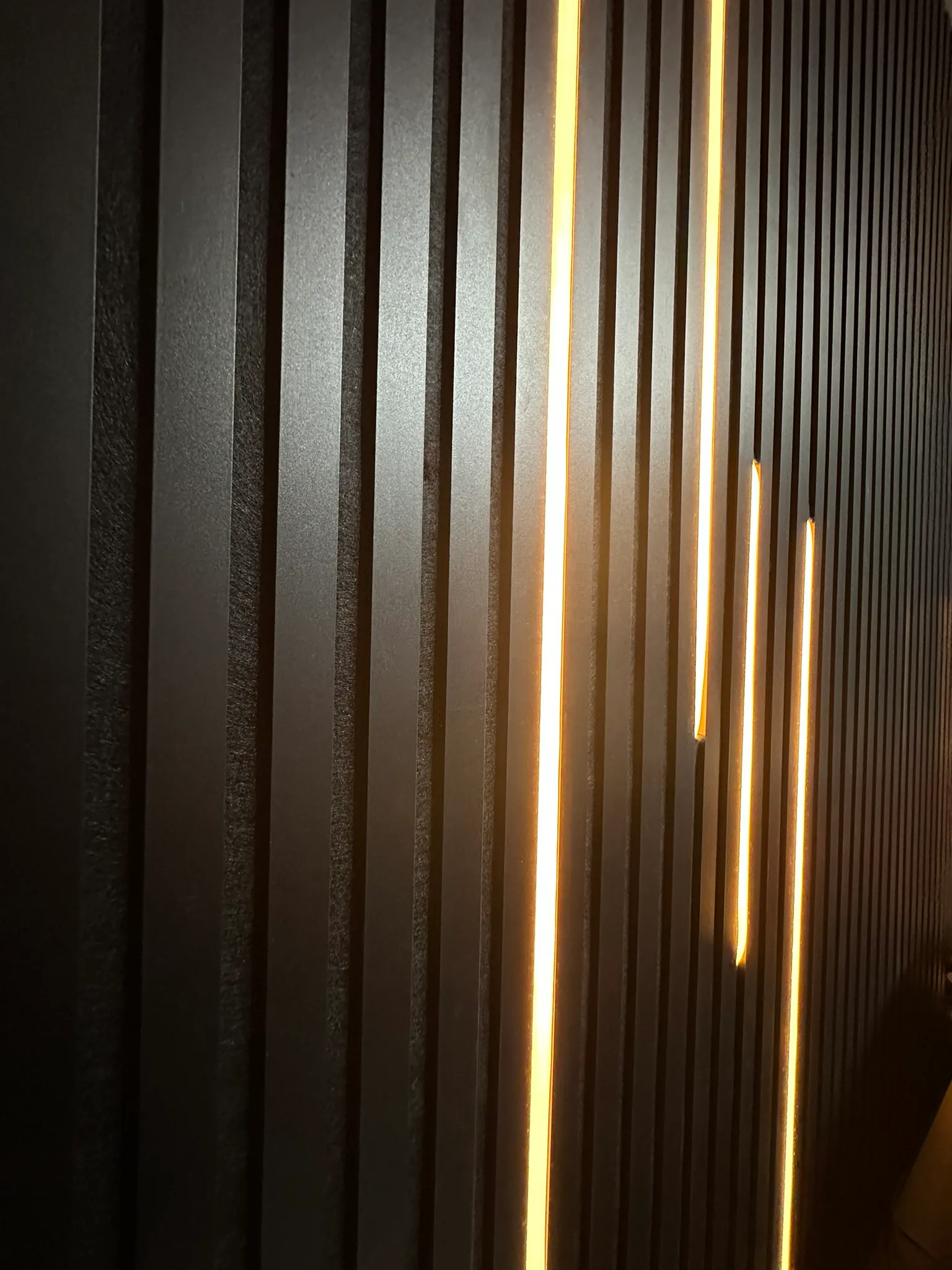 Black slatted panels with lines of warm light set into the gaps between the slats.