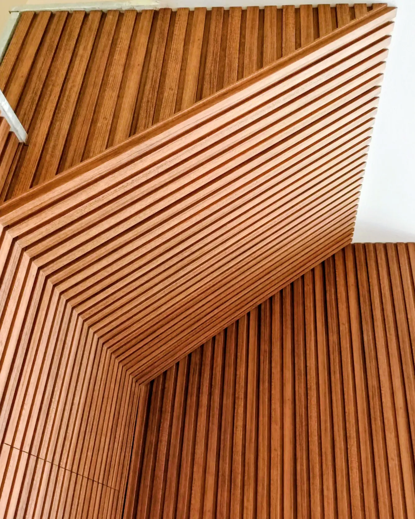 A slatted wooden ceiling meeting the wall, the slats fanning out as the angle changes.