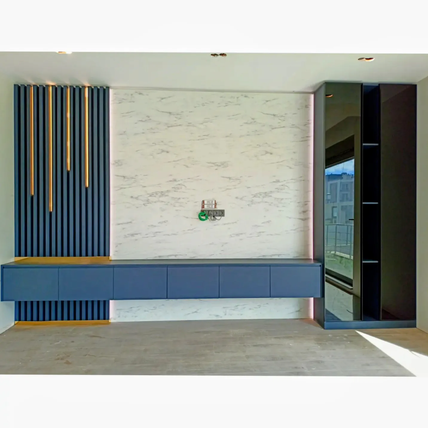 A media wall built into the room: dark slats, pale stone and a run of low storage.
