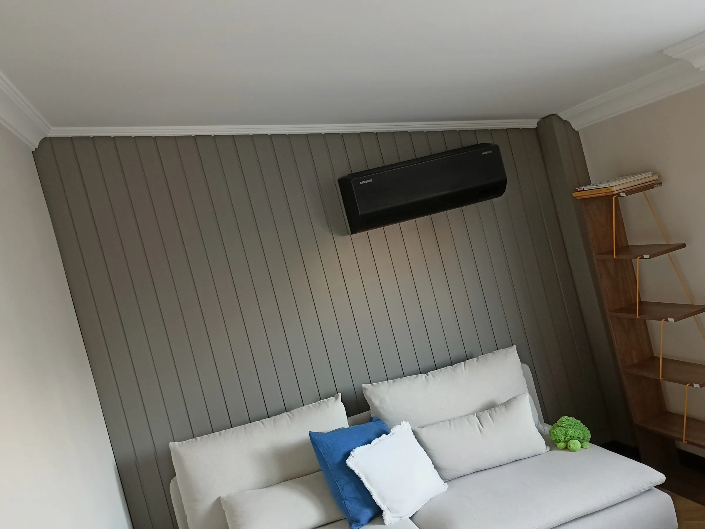 A grey slatted wall behind a bed, with air conditioning above it and a wardrobe alongside.