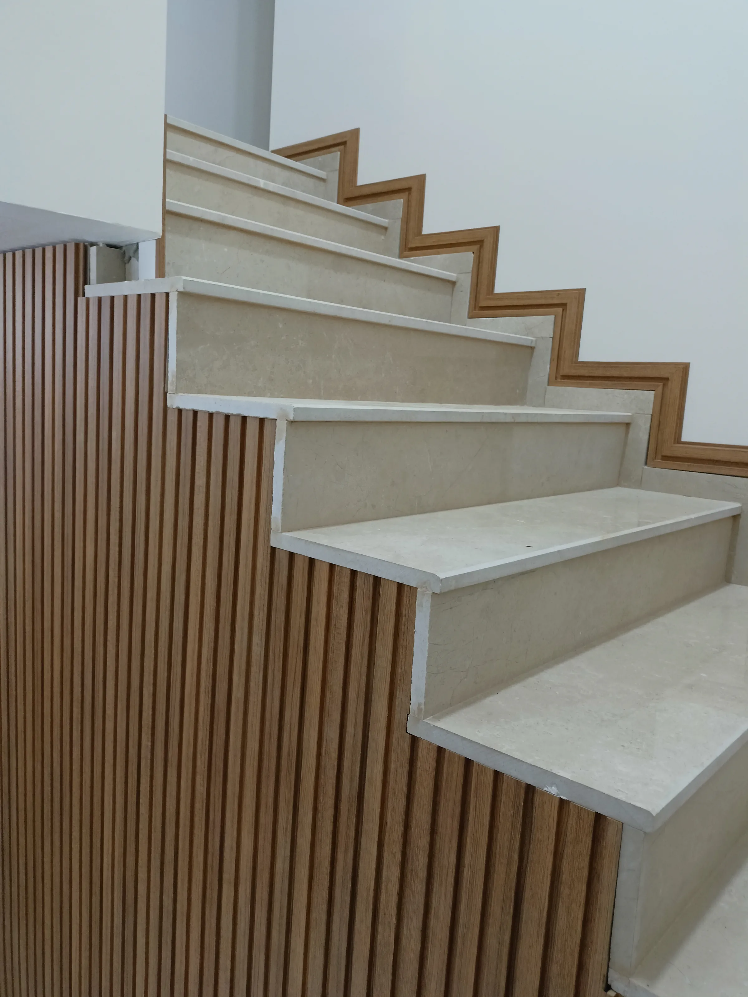 Wooden slats climbing beside stone treads, following the line of the stair.